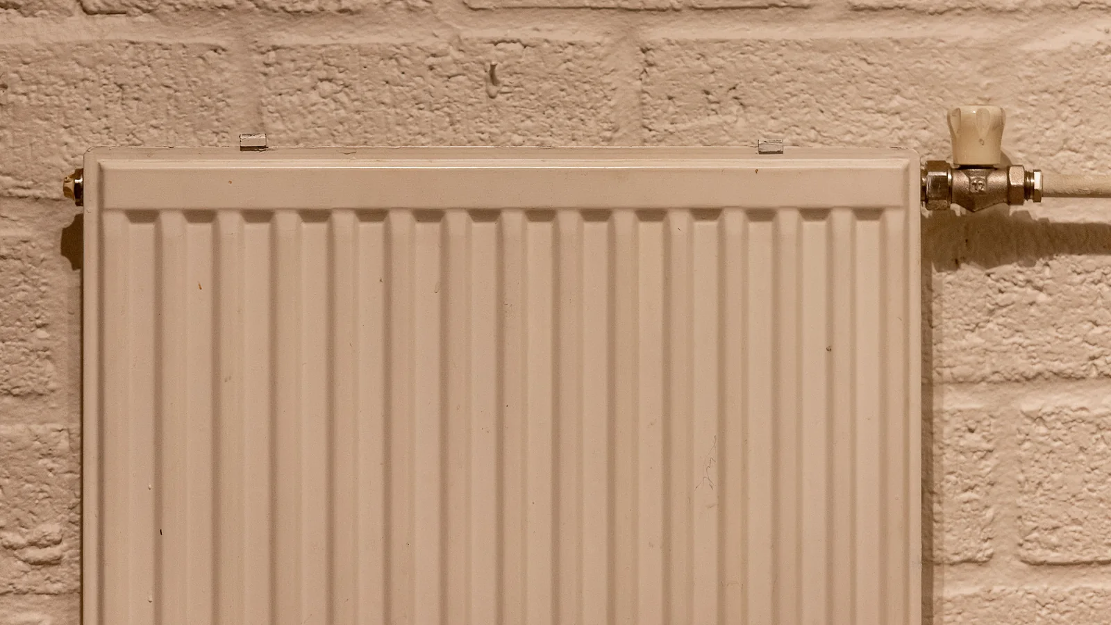 Detail eines weißen Heizkörpers mit Rohrleitung an einer Wand.