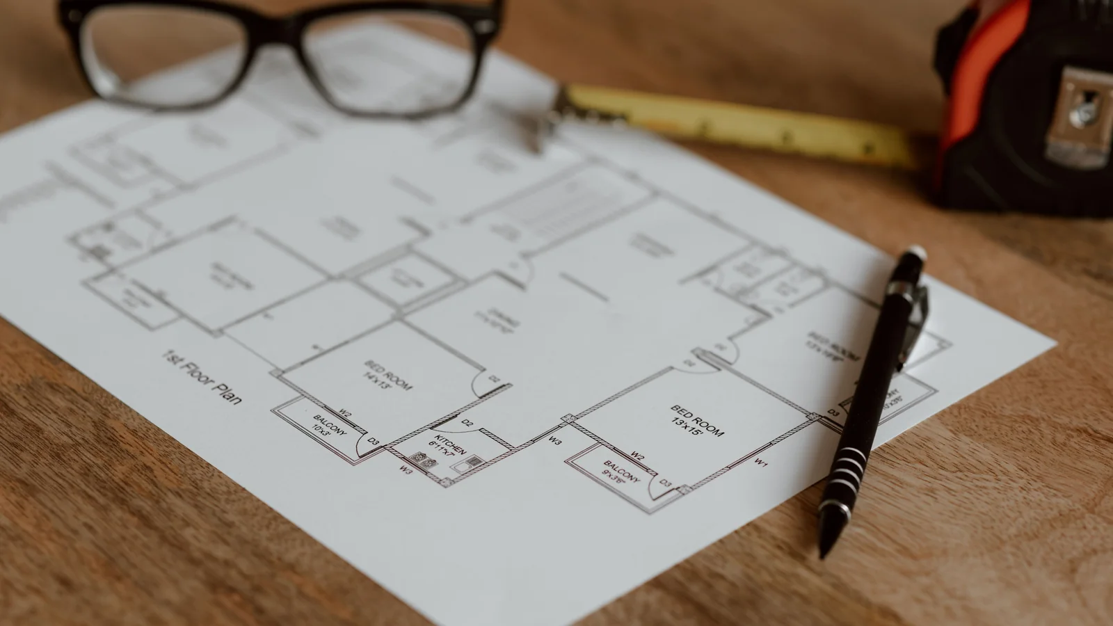 Hausgrundriss mit Stift, Lineal und Brille auf einem Tisch.