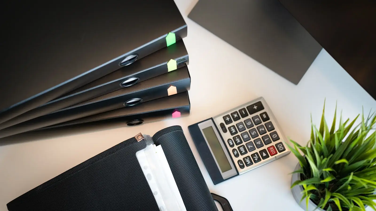 Aktenordner, Taschenrechner und Büromaterial auf einem Schreibtisch.