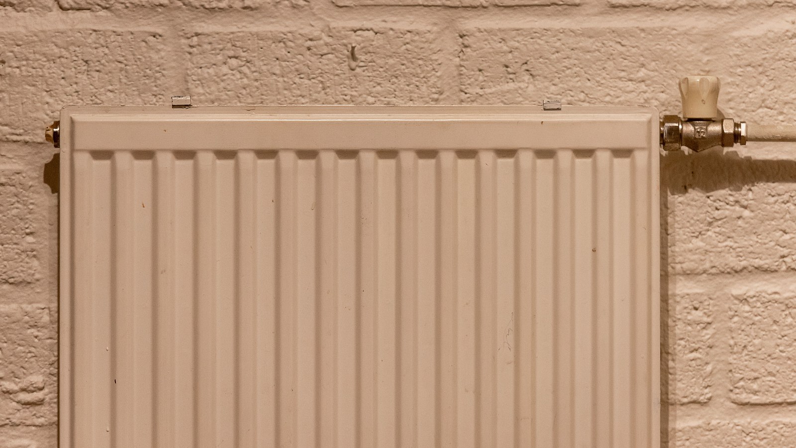Detail eines weißen Heizkörpers mit Thermostat an einer hellen Wand.